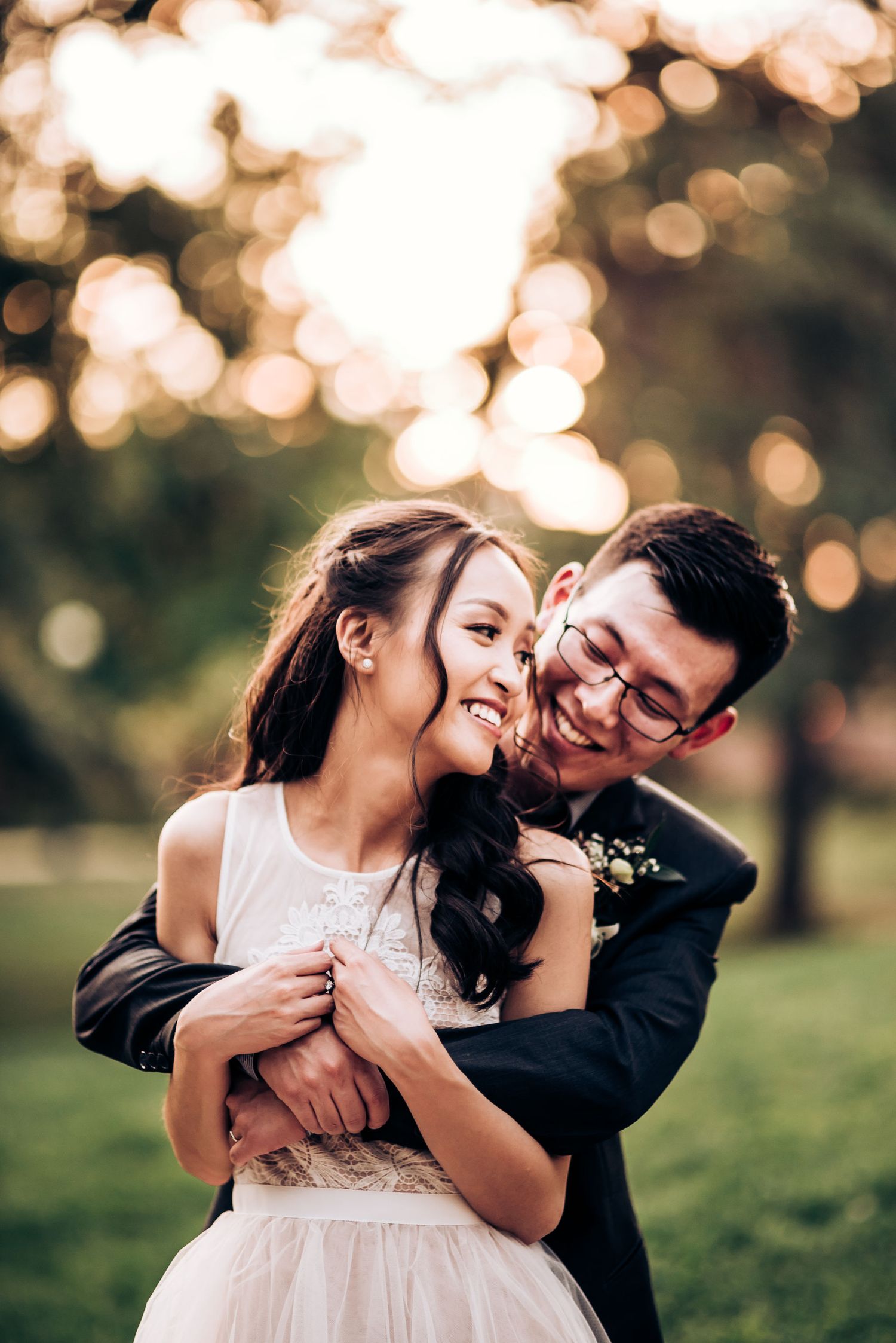 Intimate wedding portrait of couple embracing with golden bokeh lighting in outdoor setting.