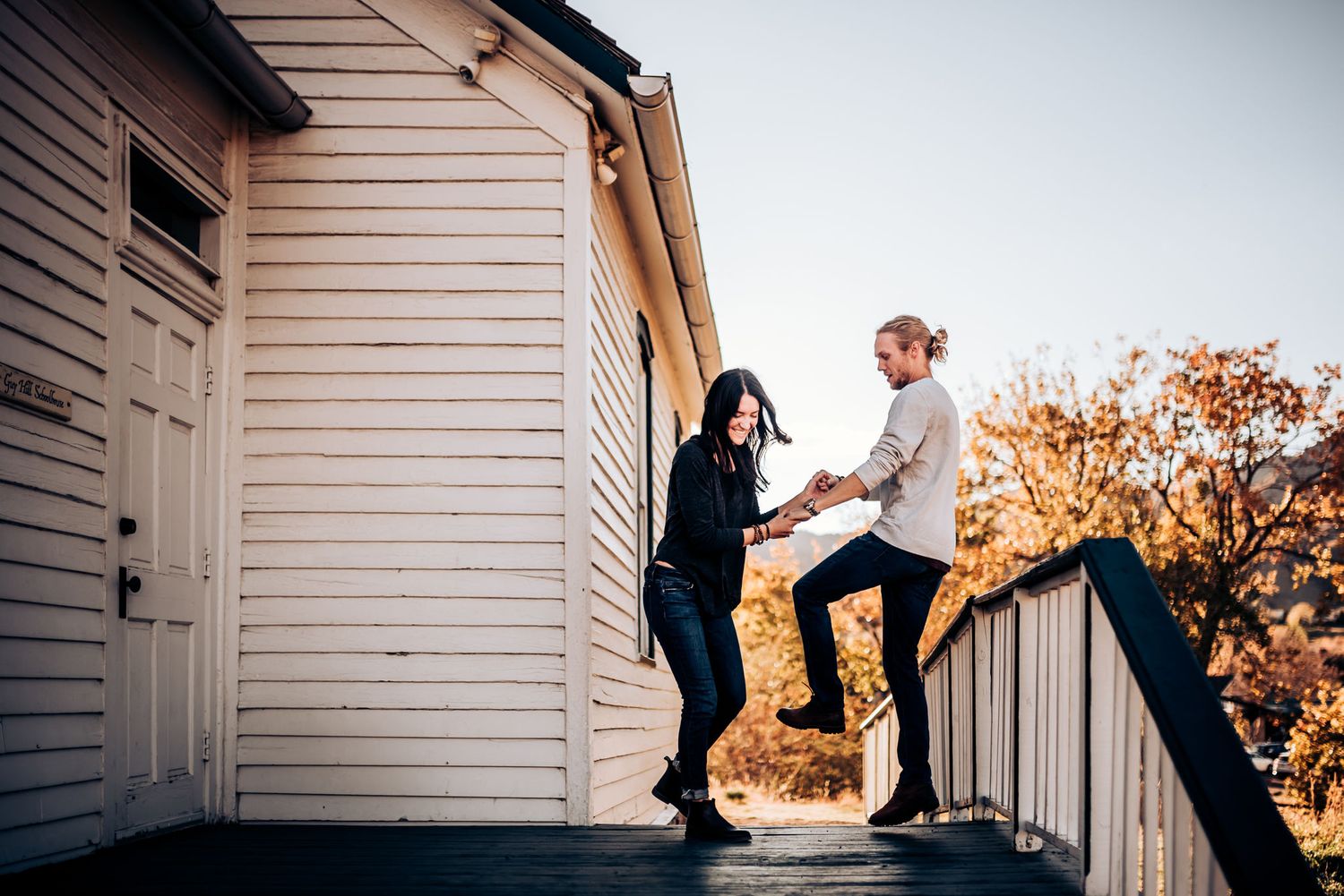 A couple holds hands while balancing on white house porch railings.