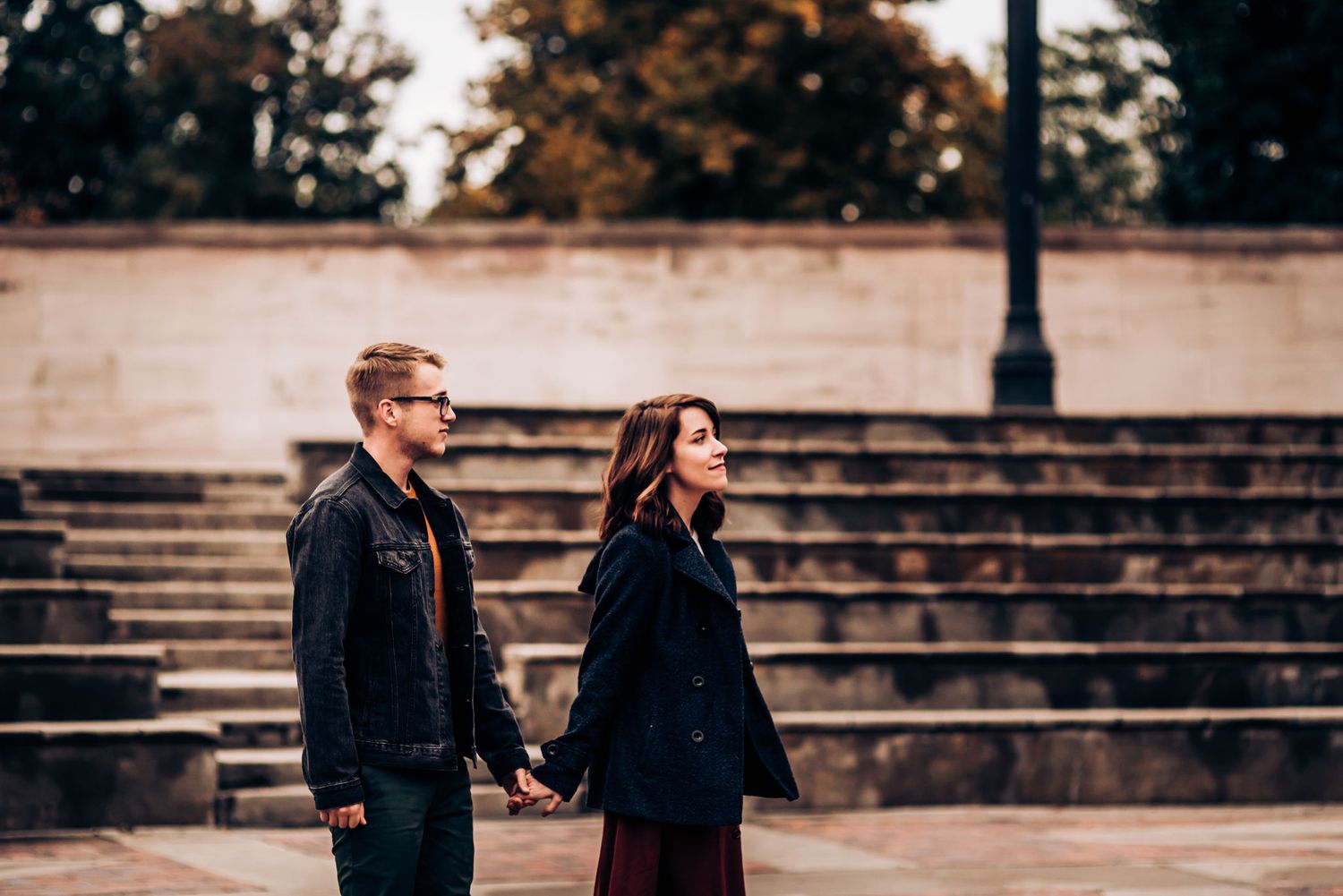 A couple holding hands stands together on stone steps during an autumn afternoon.