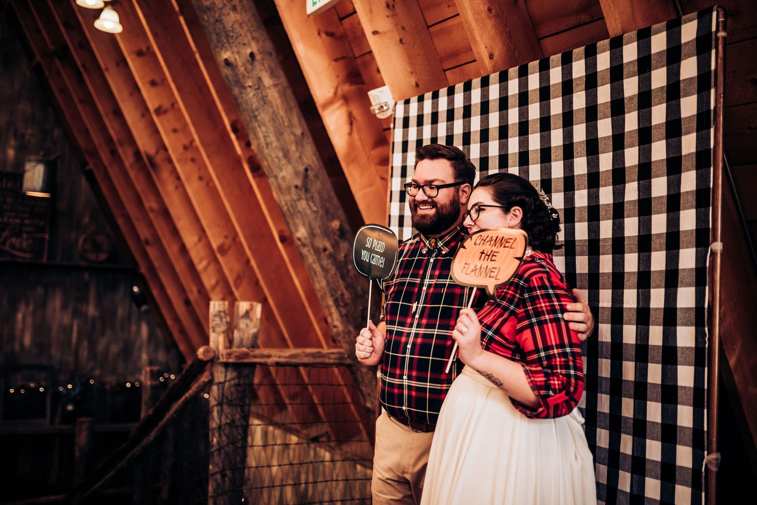 A couple celebrates at their wedding reception in a rustic barn with buffalo check backdrop.