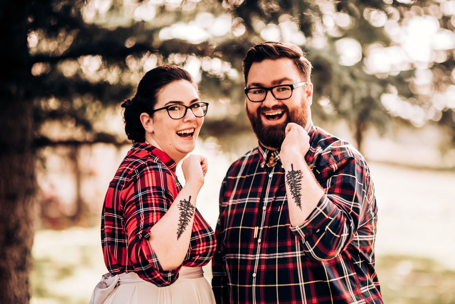 A joyful couple in matching red plaid shirts share a laugh during their outdoor photoshoot.