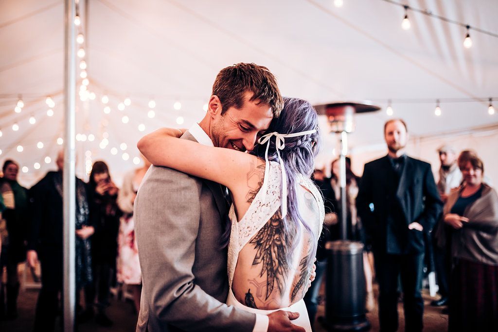 Romantic first dance captured under twinkling lights in wedding tent.