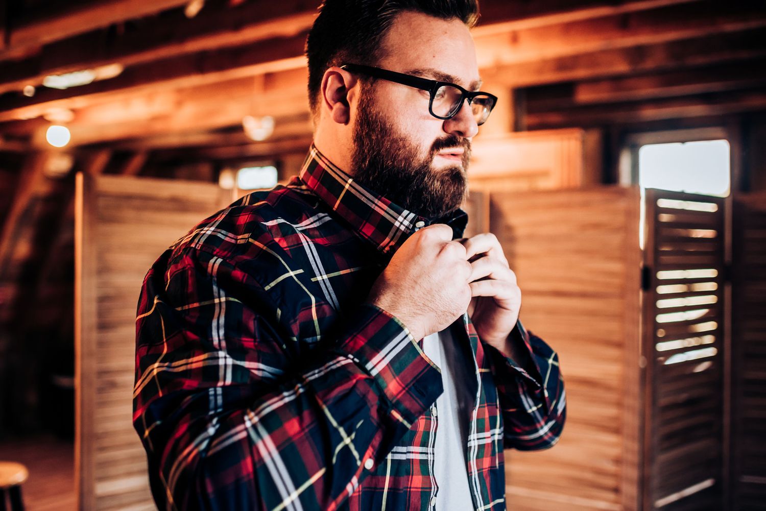 A plaid shirt and glasses create a stylish rustic portrait in warm lighting.