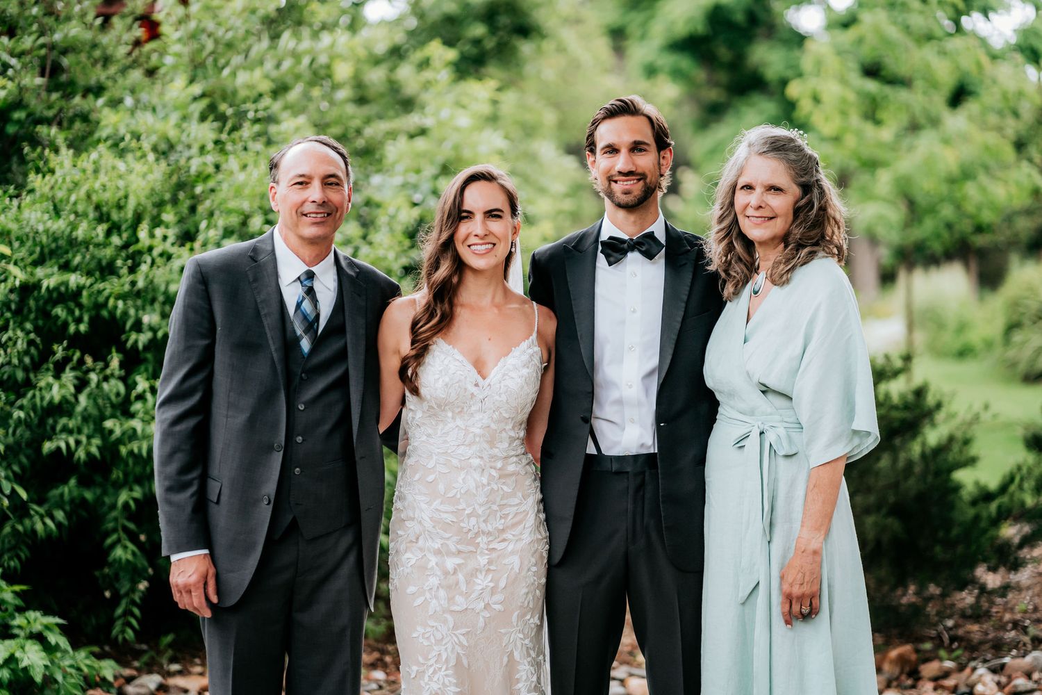 A formal wedding portrait taken outdoors with lush greenery in the background.