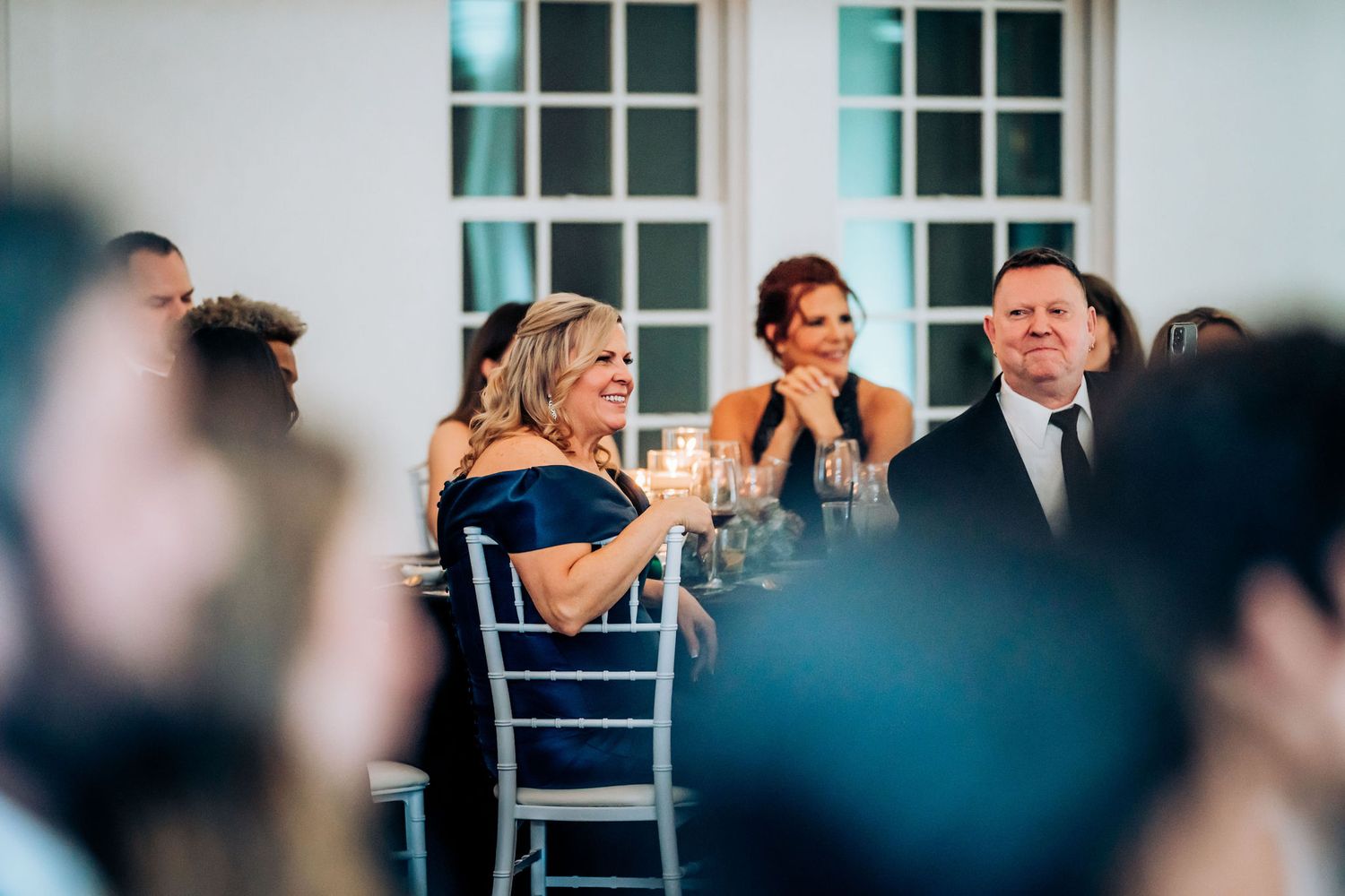 Wedding guests react emotionally during reception speeches while seated at decorated tables.