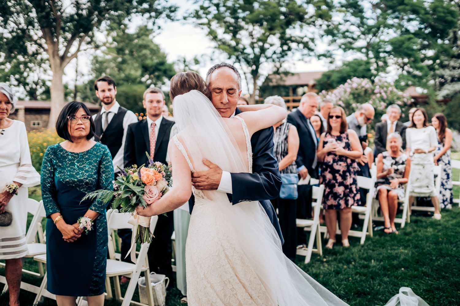 Emotional wedding ceremony moment on lawn with guests seated in white chairs during outdoor celebration.
