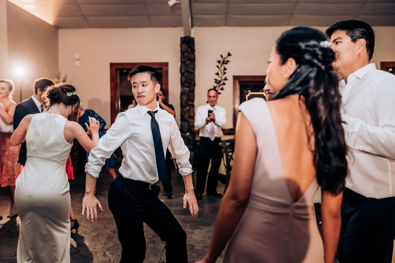 Wedding guests dance enthusiastically on the reception dance floor under warm lighting.