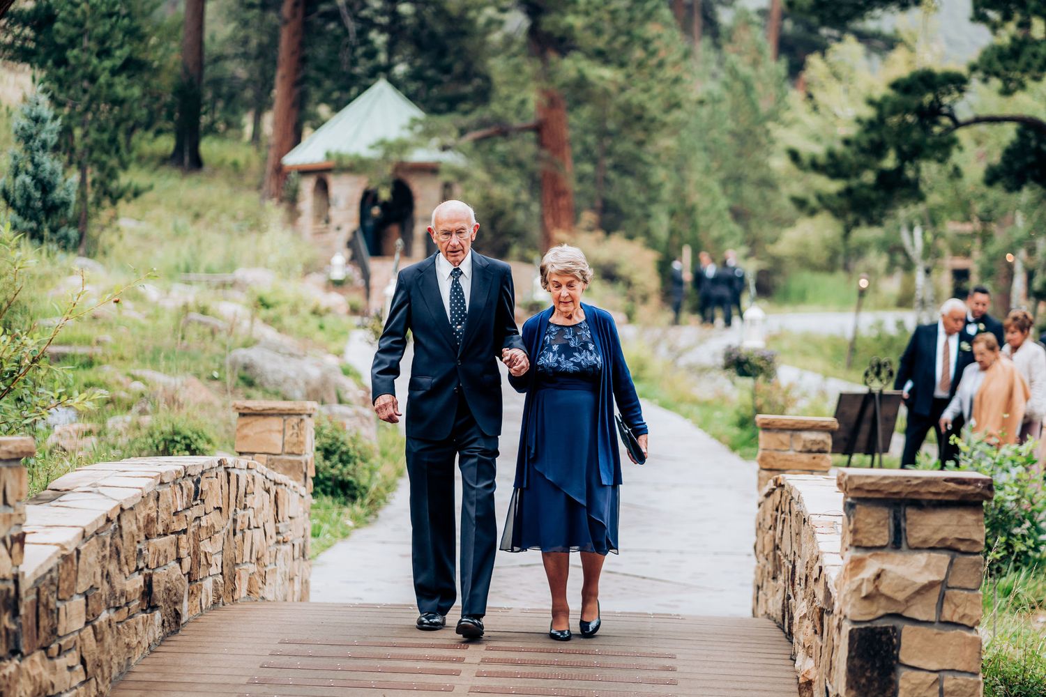 Couple walking together on stone bridge pathway at outdoor mountain venue.