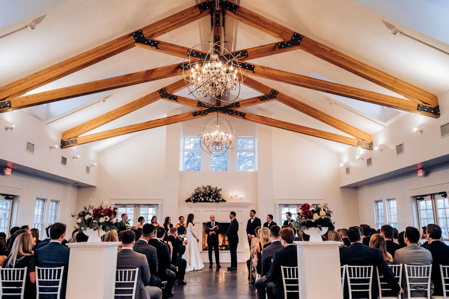 Wedding reception venue with exposed wooden beams and crystal chandelier filled with guests.