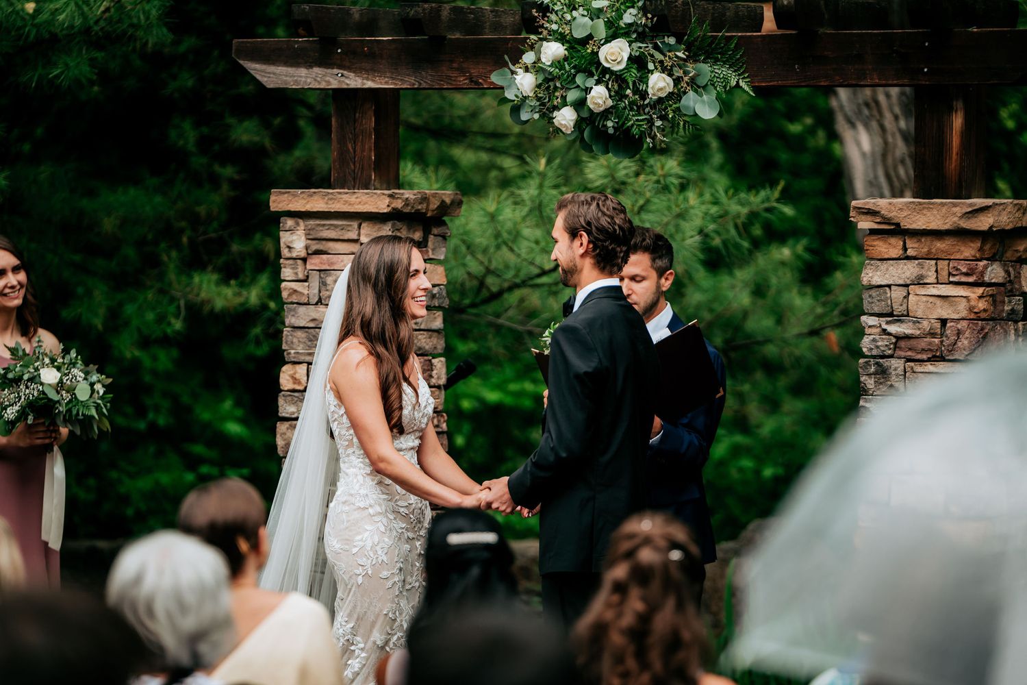 A wedding ceremony under a stone archway decorated with white floral arrangements.