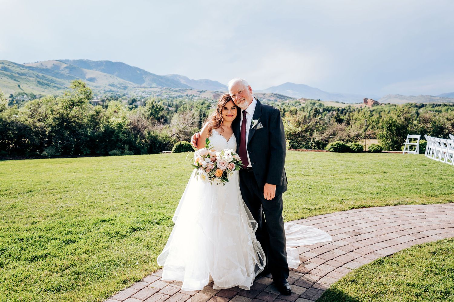 Bride and father share a special moment on brick pathway with mountain backdrop.