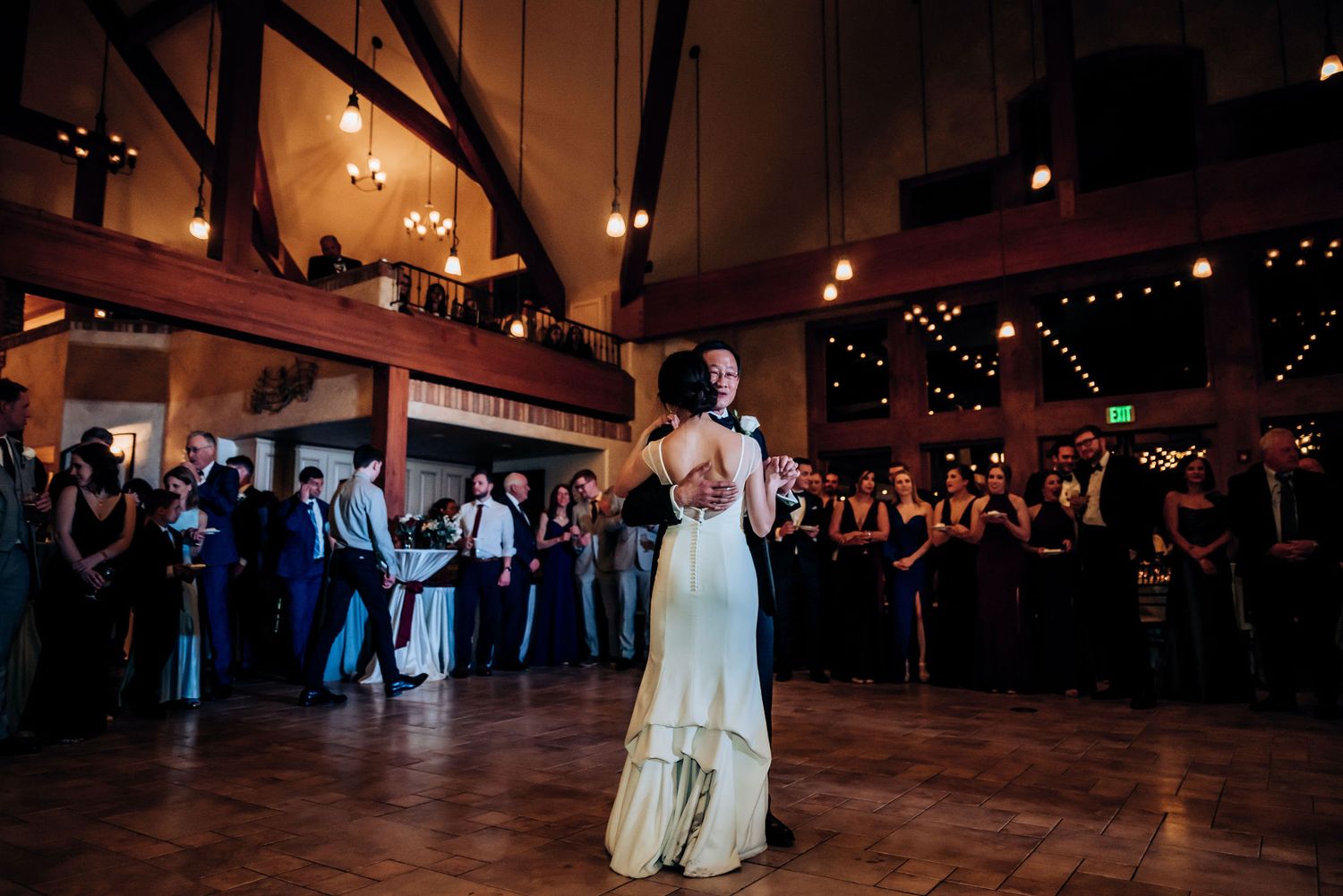 A wedding dance moment captured in a dimly lit ballroom with watching guests.
