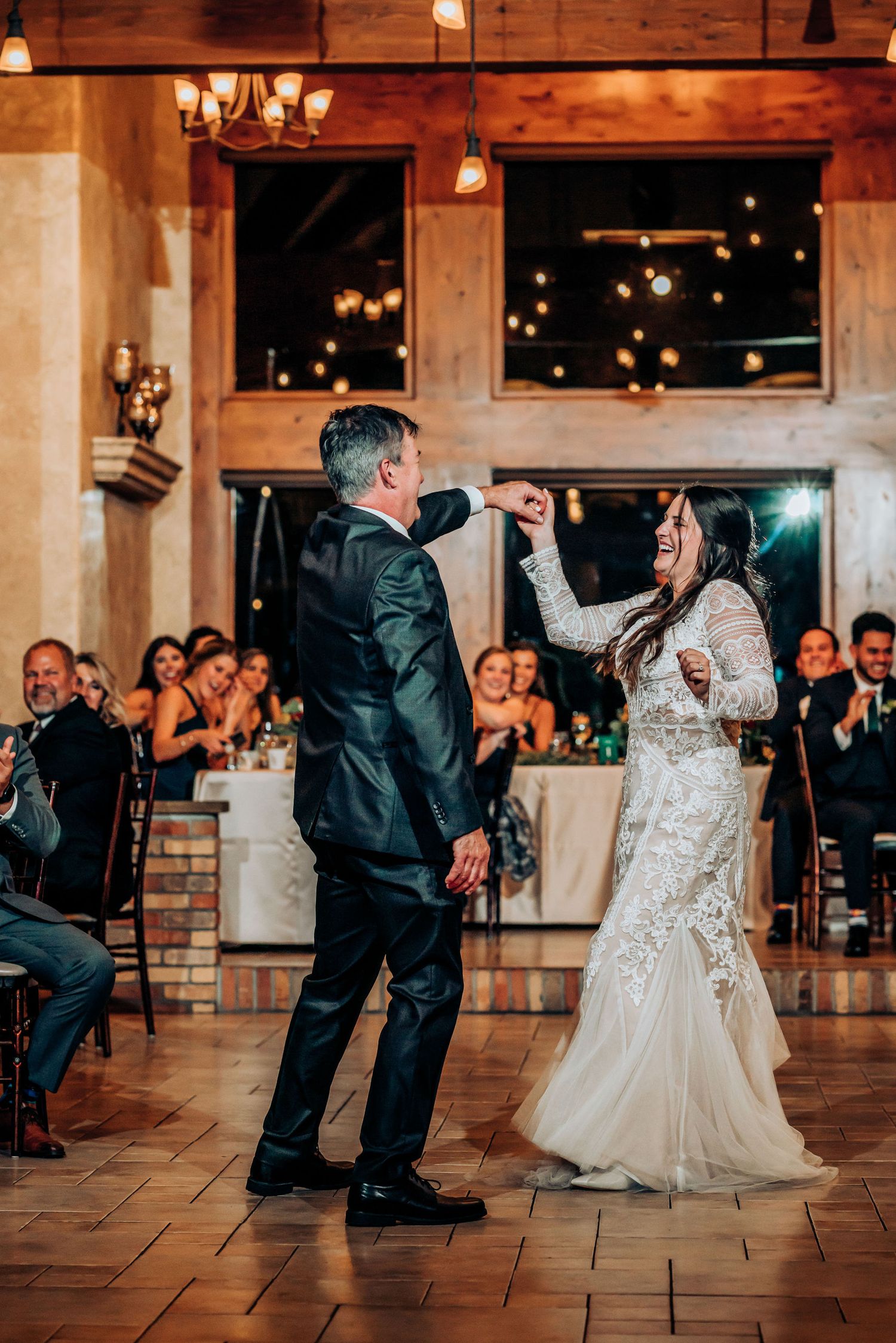 Couple dances together on a tiled floor during their wedding reception with fairy lights in the background.