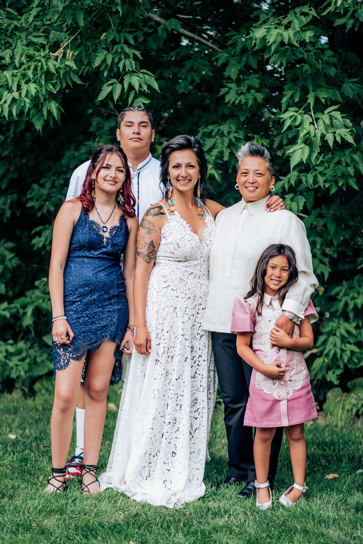 Wedding group portrait of a family in formal attire against a leafy green background.