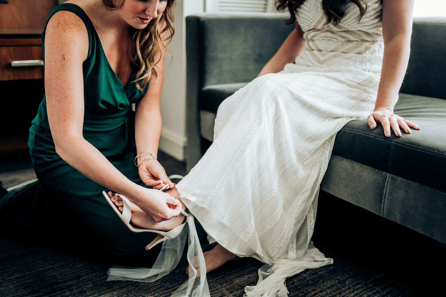 Person helping adjust white formal dress while sitting on steps.