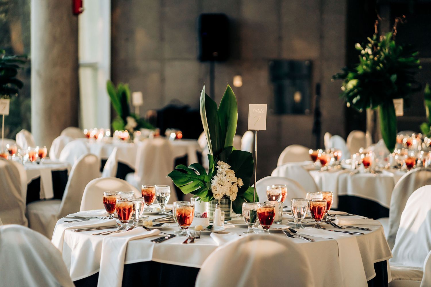 Wedding reception venue with white tablecloths and tropical floral arrangements.