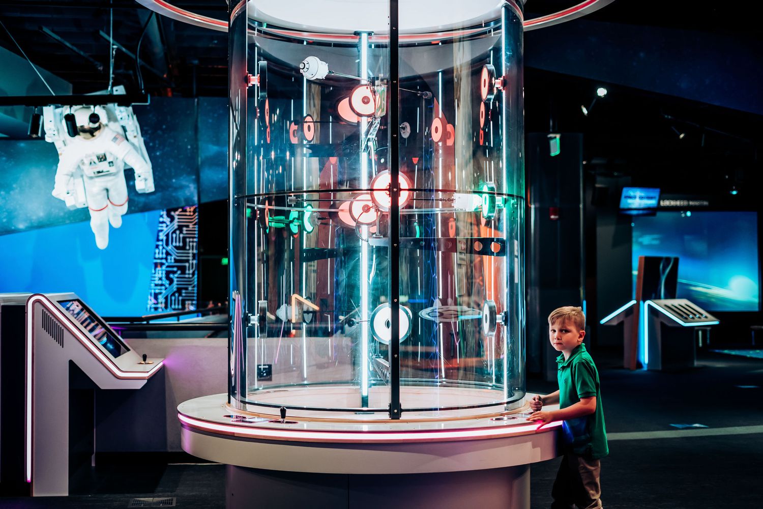 Interactive science museum display featuring space suits and cylindrical glass chamber with neon lighting.