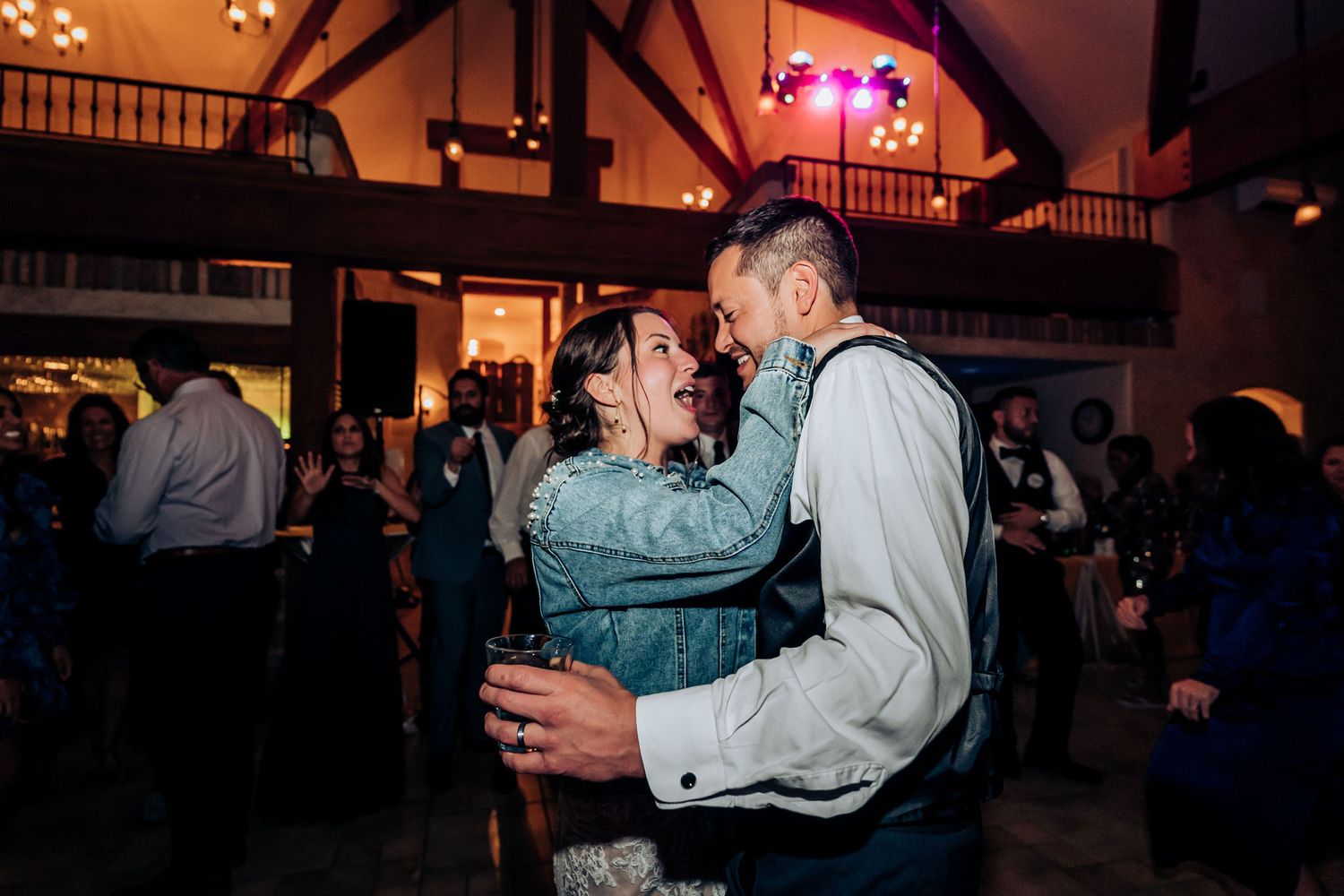 Couple sharing a joyful dance moment in a warmly lit rustic reception venue.
