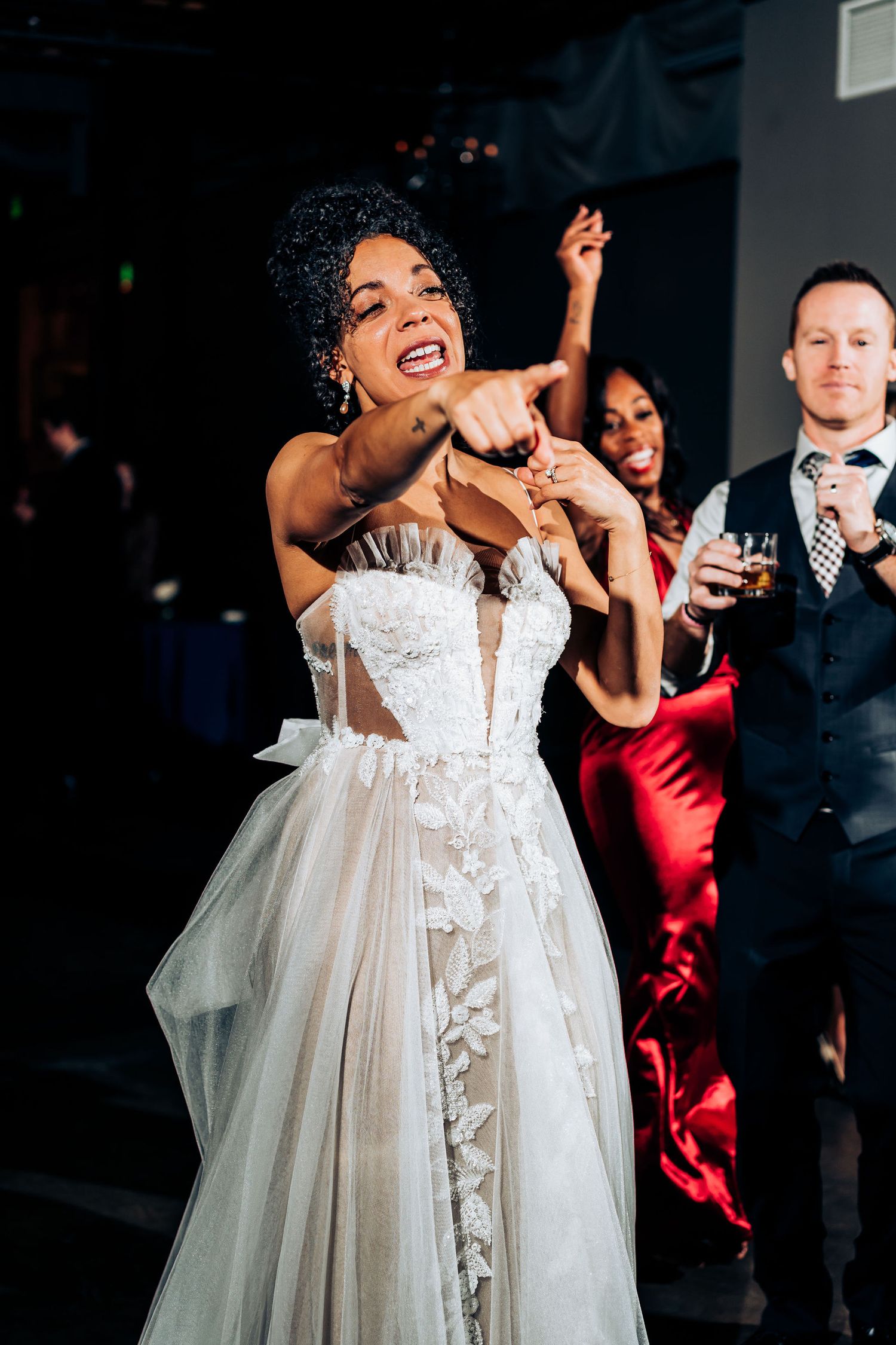 A bride in a white lace wedding dress dances joyfully at her reception celebration.