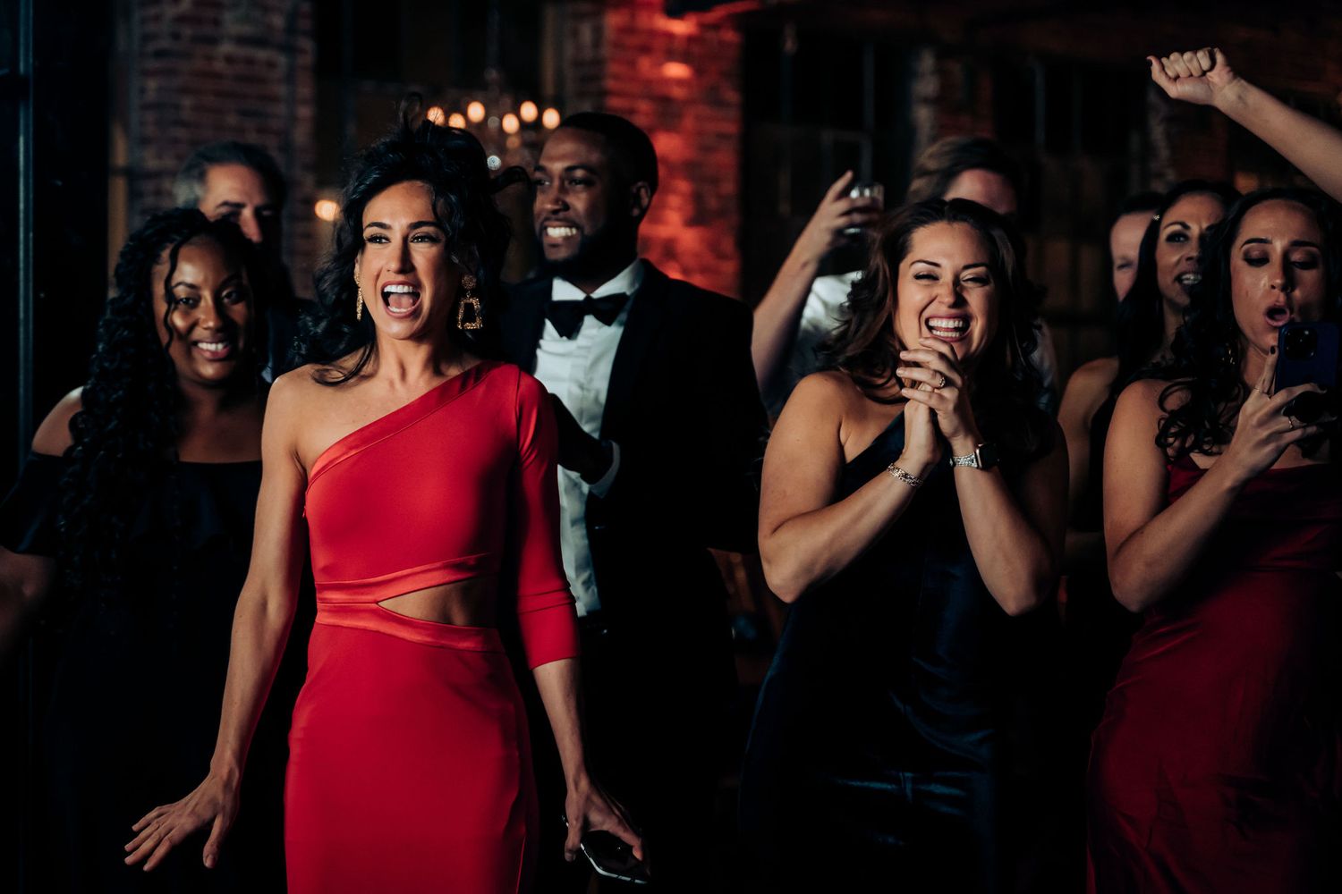 Wedding guests in colorful formal attire dance and celebrate at a reception.