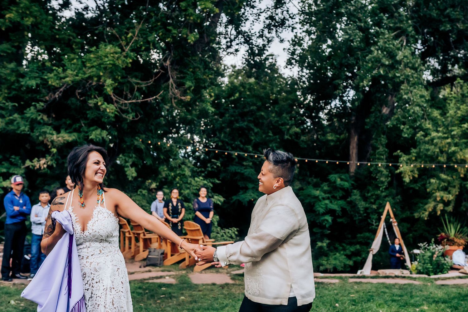 Celebratory dance moment during an outdoor wedding with a wooden arch structure visible in background.