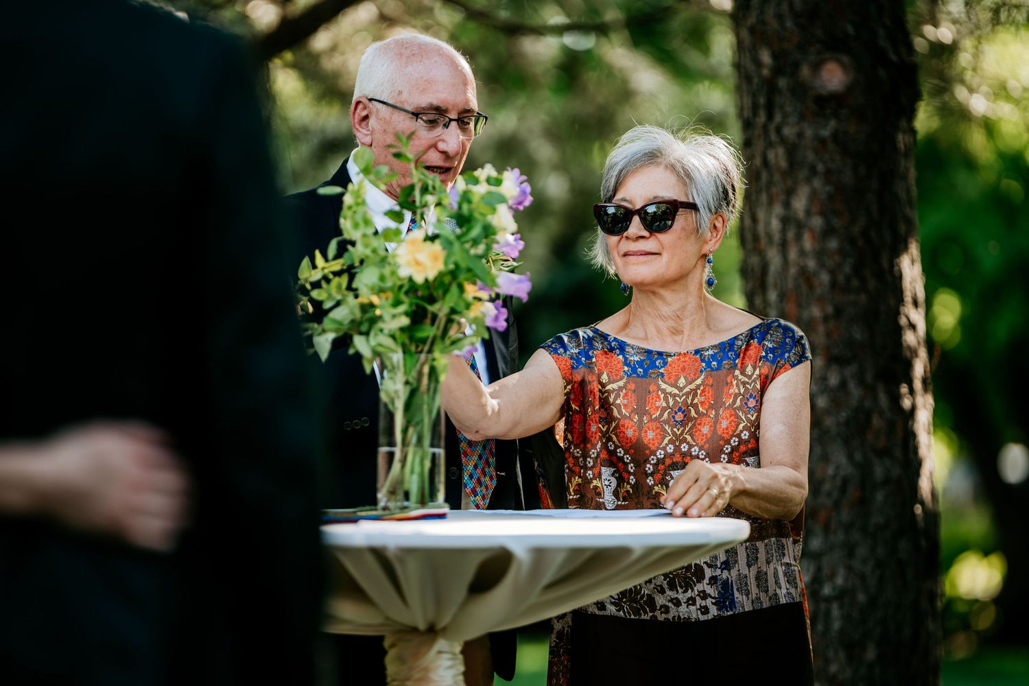Two guests arrange flowers at an outdoor table during a formal event.