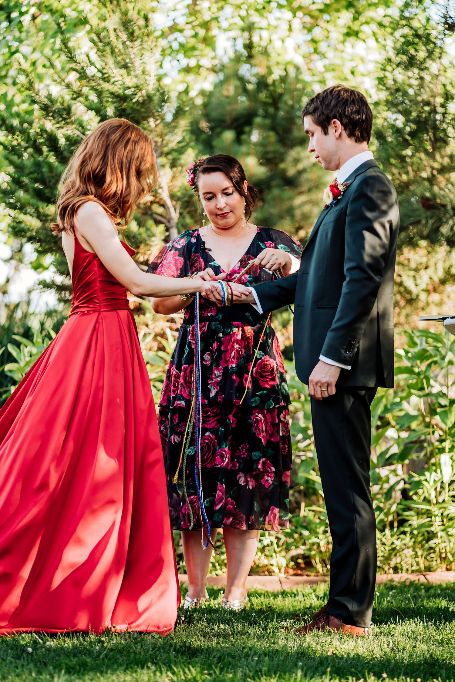 Wedding participants gather on a garden path during an outdoor ceremony.