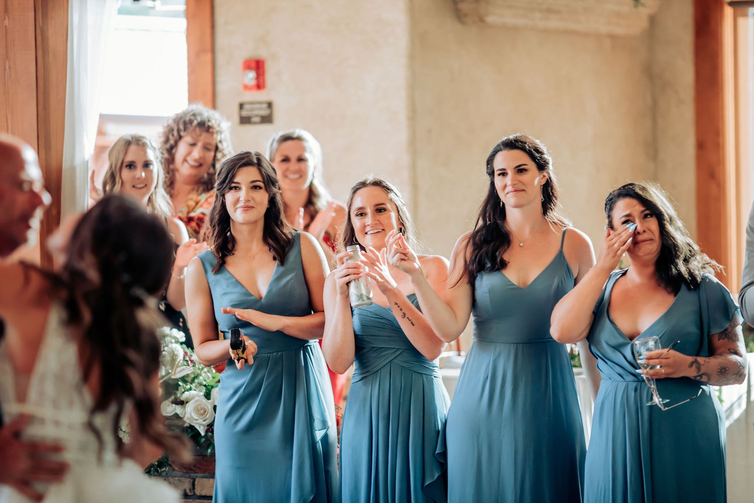 Bridesmaids in matching blue dresses share emotional reactions during wedding festivities.
