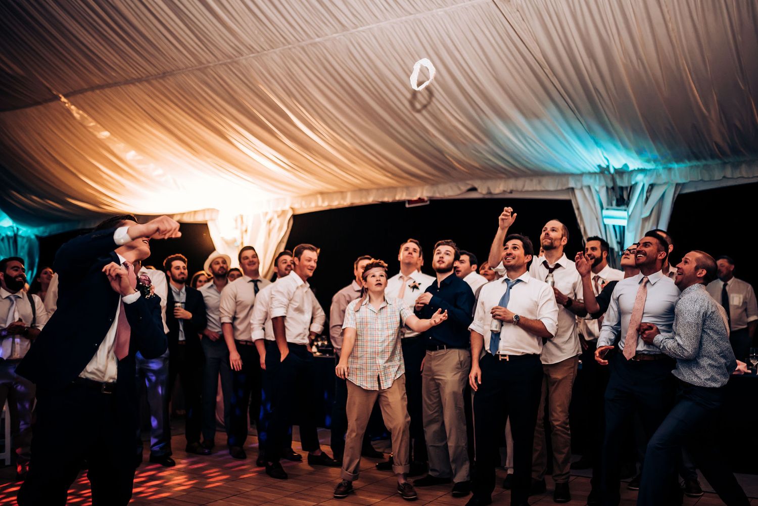 Large group of wedding guests gathered on dance floor under tent lighting.