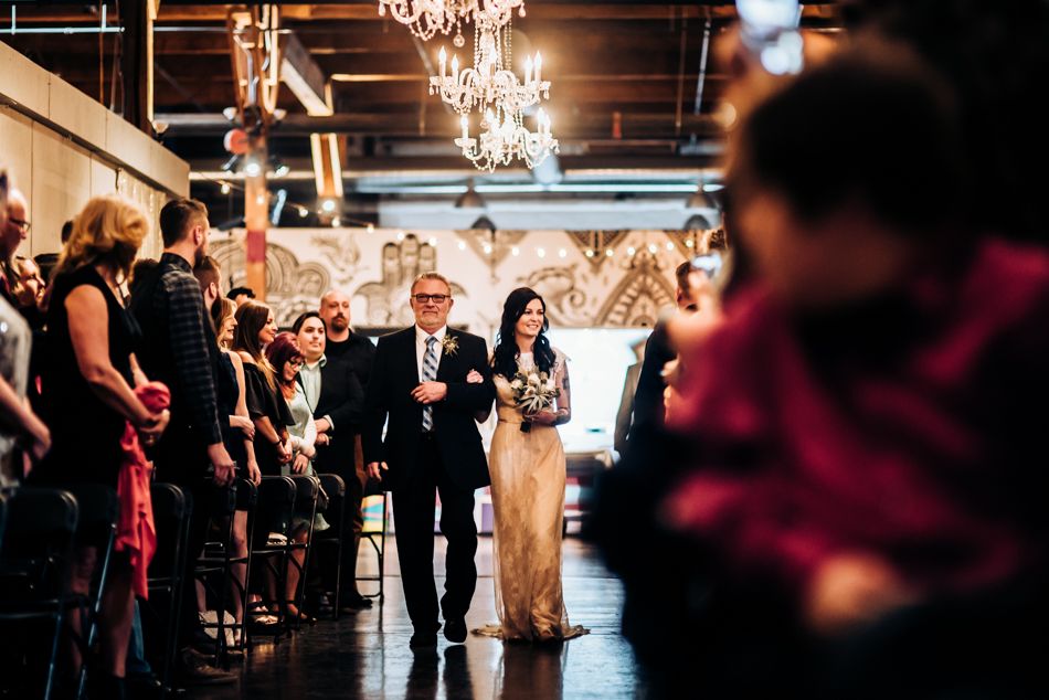 Wedding guests line both sides of an aisle as a processional takes place under elegant crystal chandeliers.