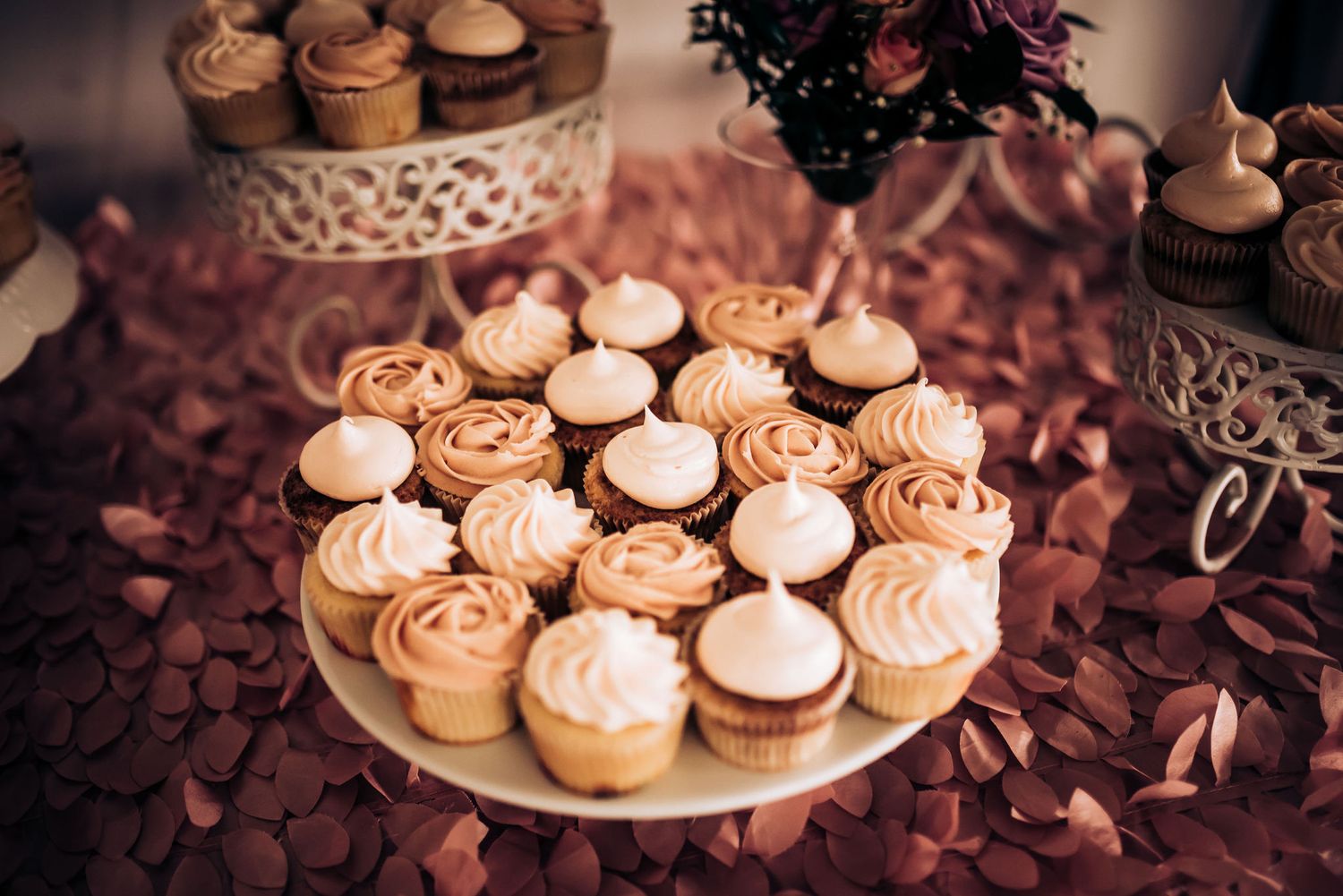 Elegant display of frosted cupcakes arranged on white decorative cake stands with rose gold accents.