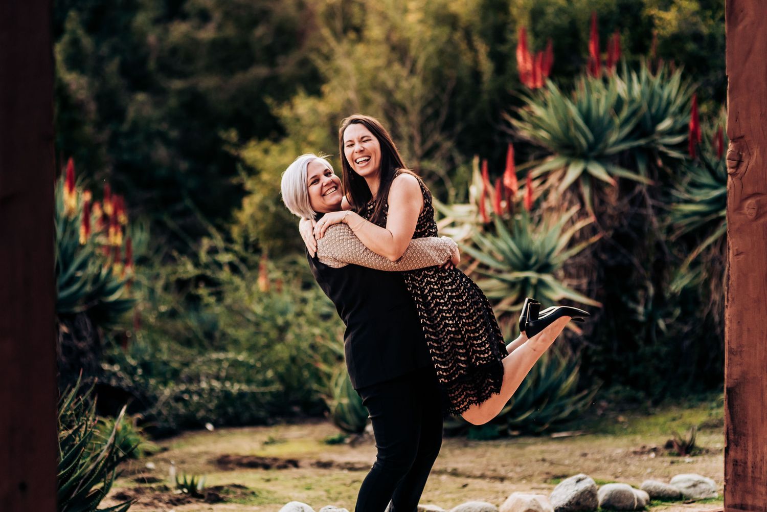 A playful lift between two people in a garden pathway surrounded by tropical plants.
