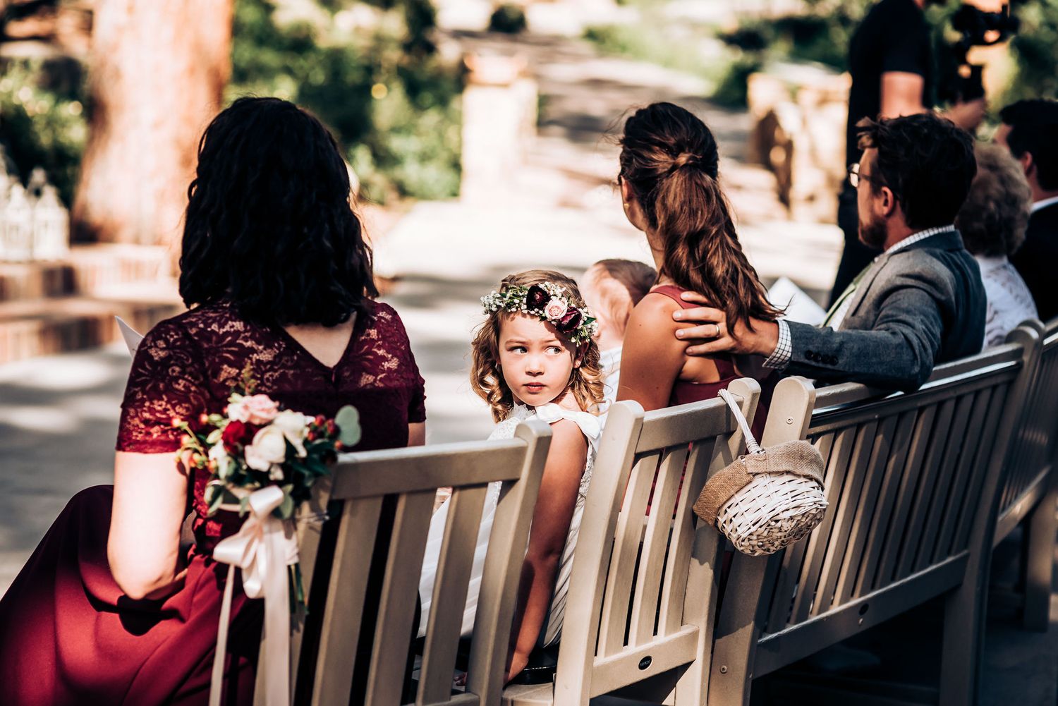Wedding guests seated on wooden benches watching the ceremony in a garden setting.