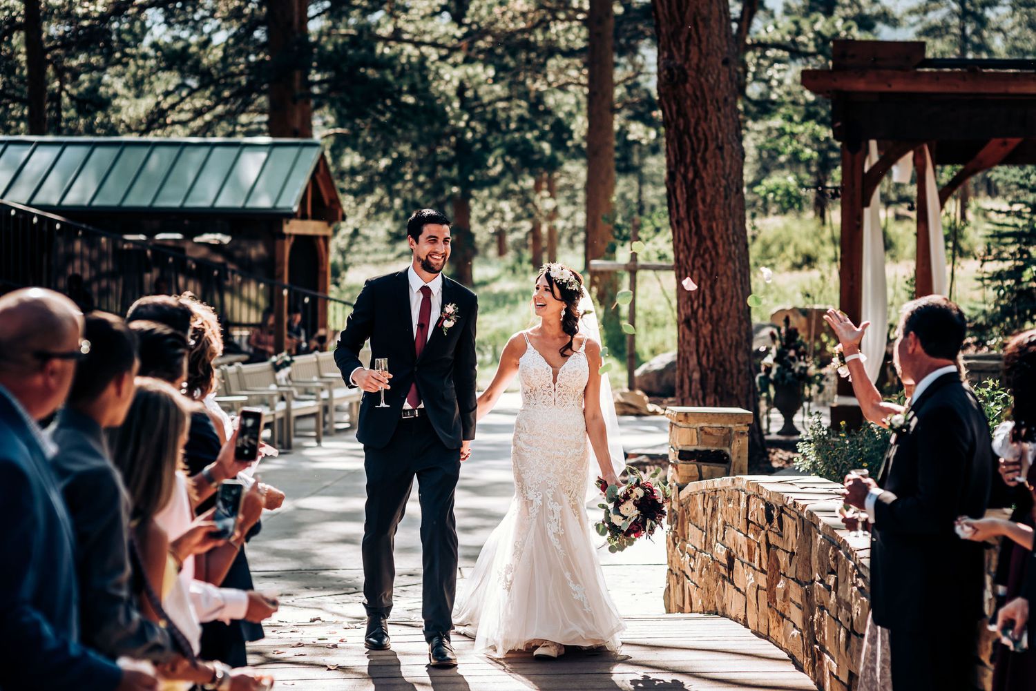 A wedding ceremony takes place in a rustic outdoor venue surrounded by pine trees.