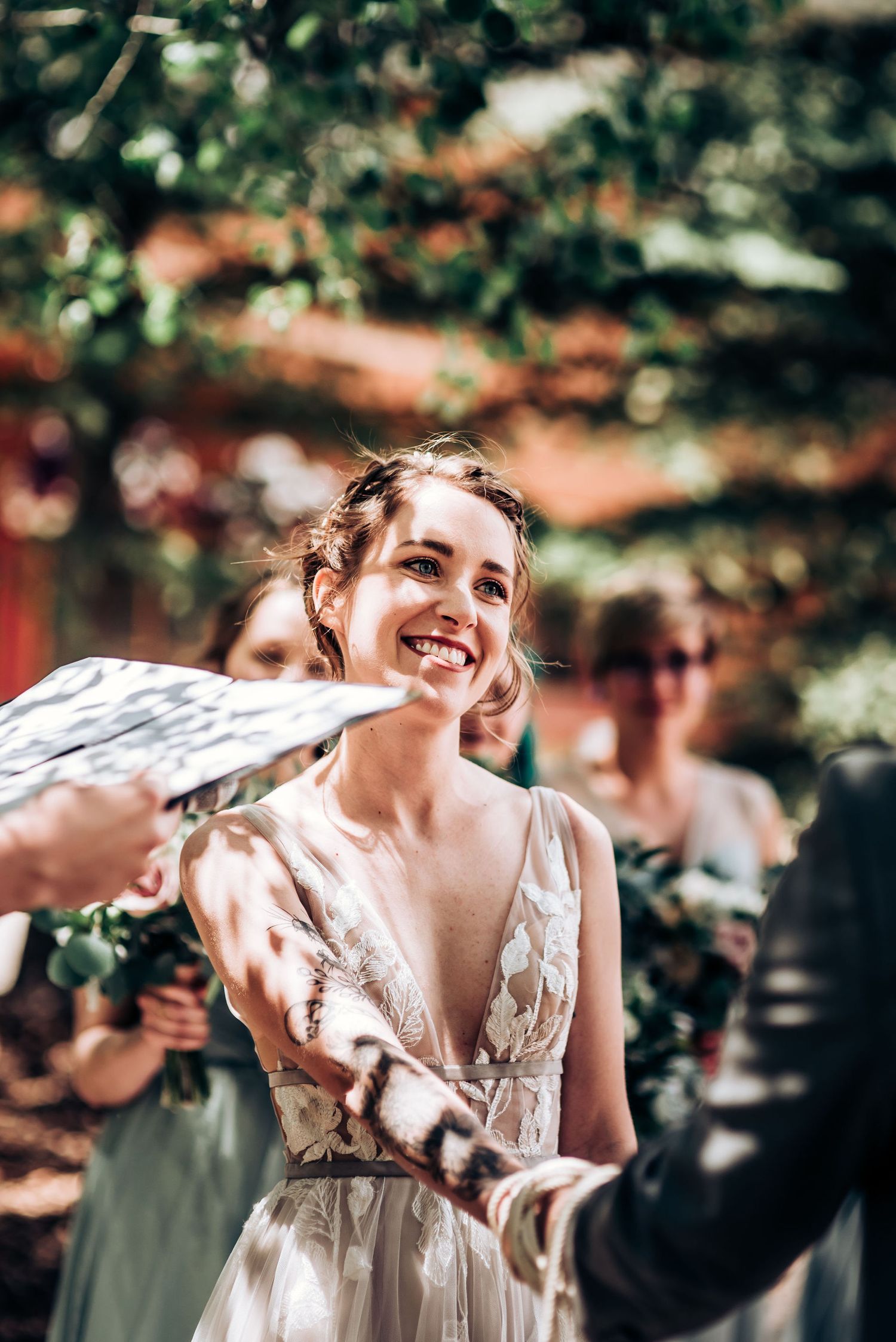 A joyful moment captured during an outdoor wedding with dappled sunlight through trees.