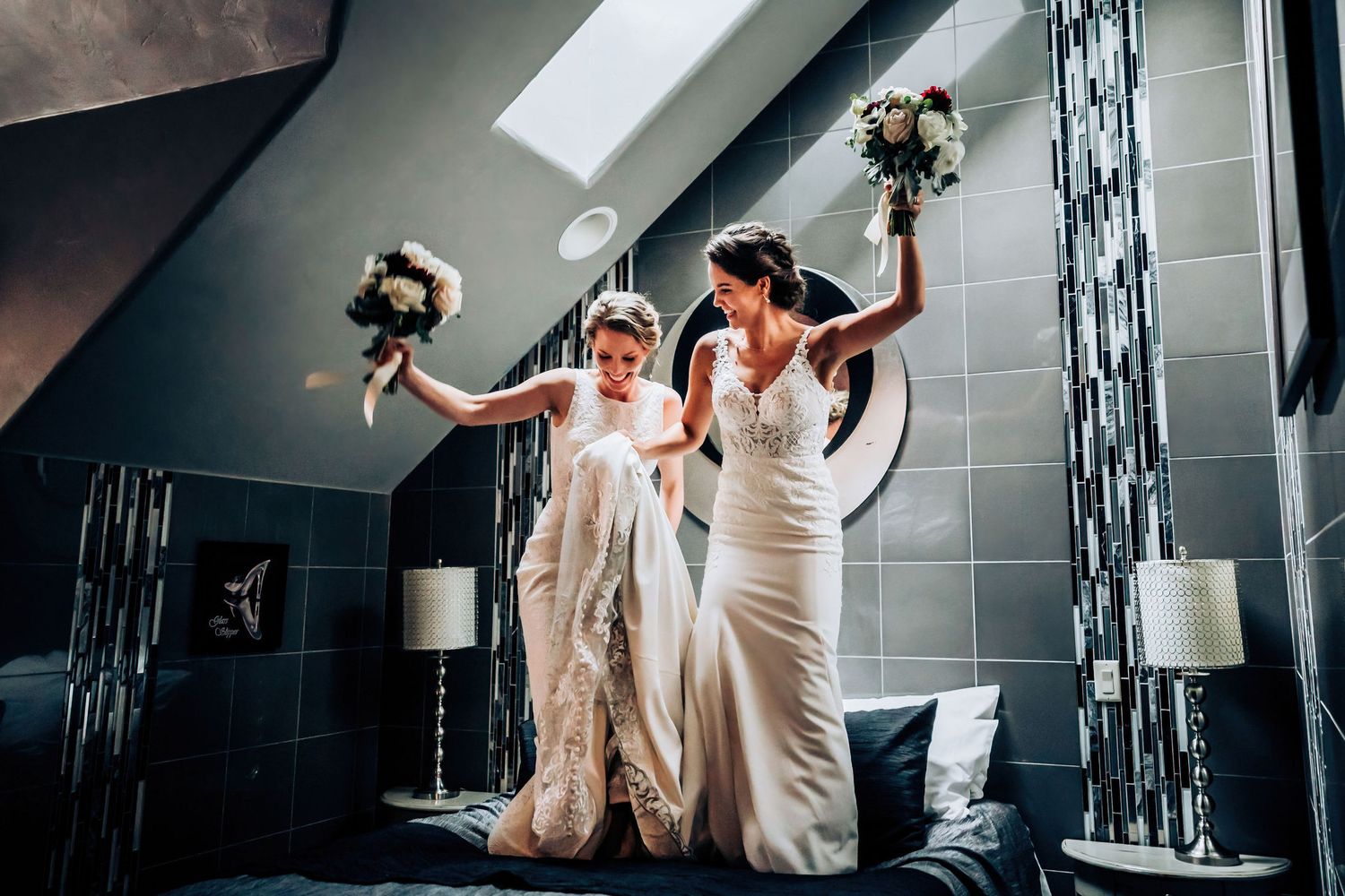 Joy-filled wedding celebration with white dresses and raised bouquets in a stylish room.