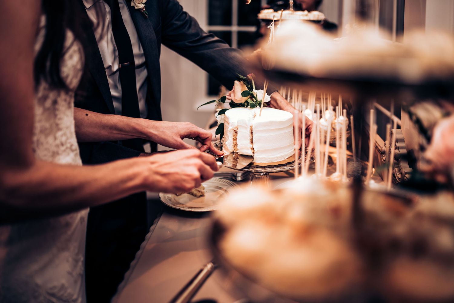 A wedding cake being cut during an indoor celebration with warm ambient lighting.