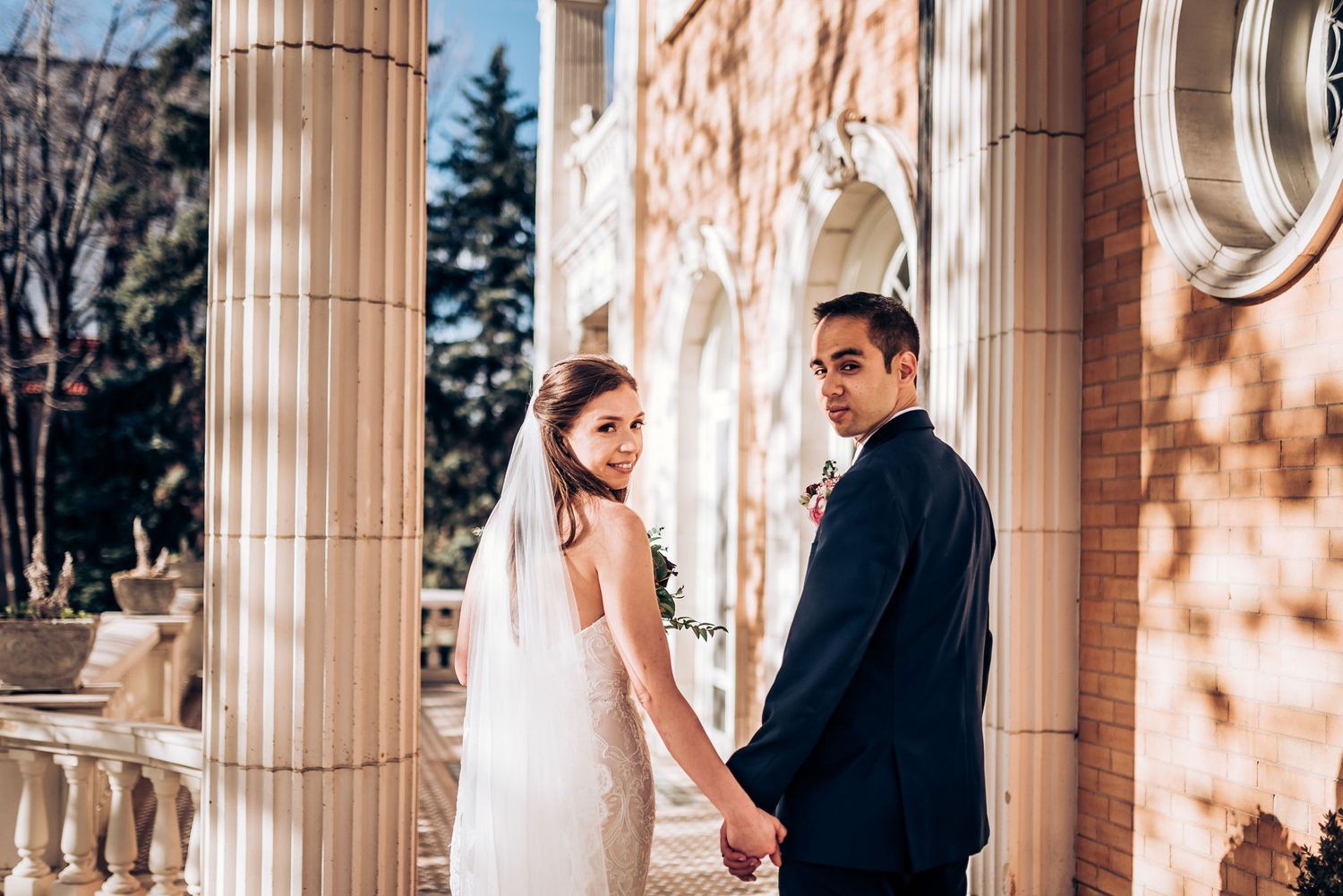 Bride and groom share tender moment on historic building's columned porch.