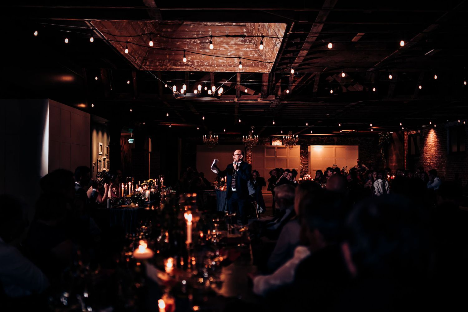 Dark reception venue illuminated by candlelight and overhead string lights.