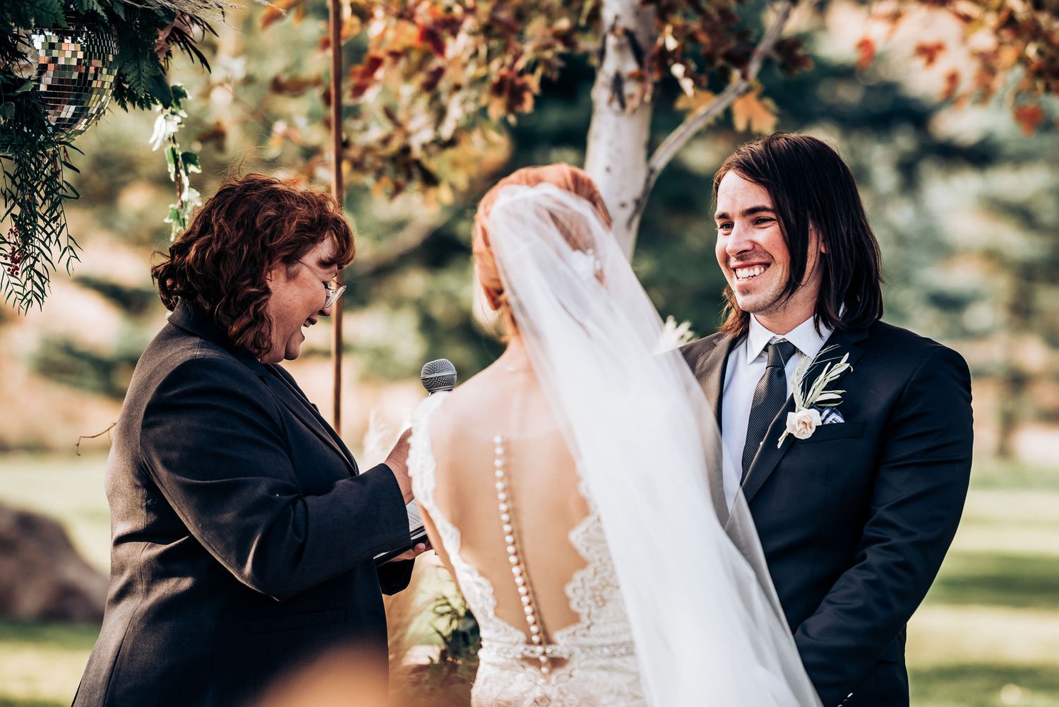 An emotional moment during an outdoor wedding ceremony with autumn foliage in the background.
