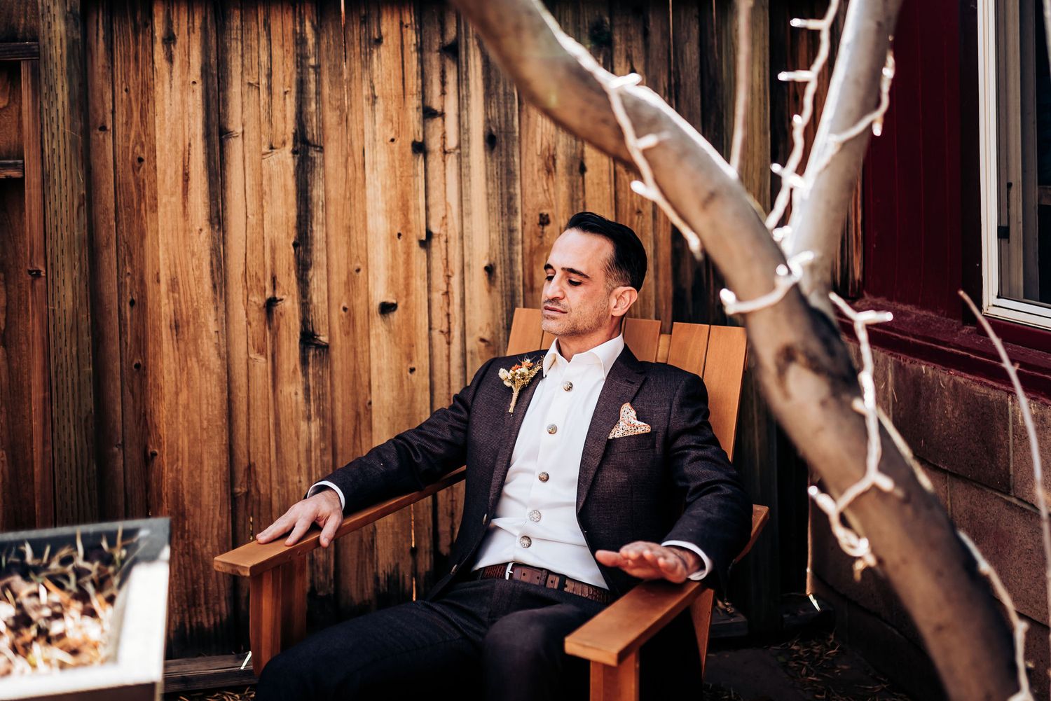 Person in formal wear seated in wooden chair with dramatic lighting.