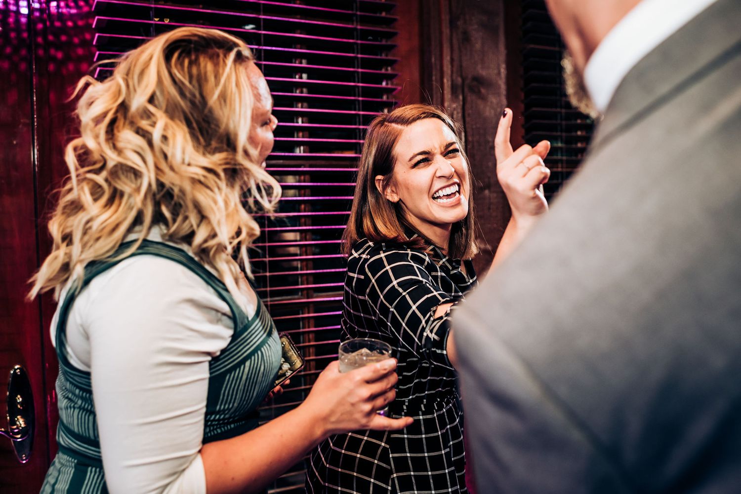 Friends sharing drinks and laughter at a stylish party with red ambient lighting.