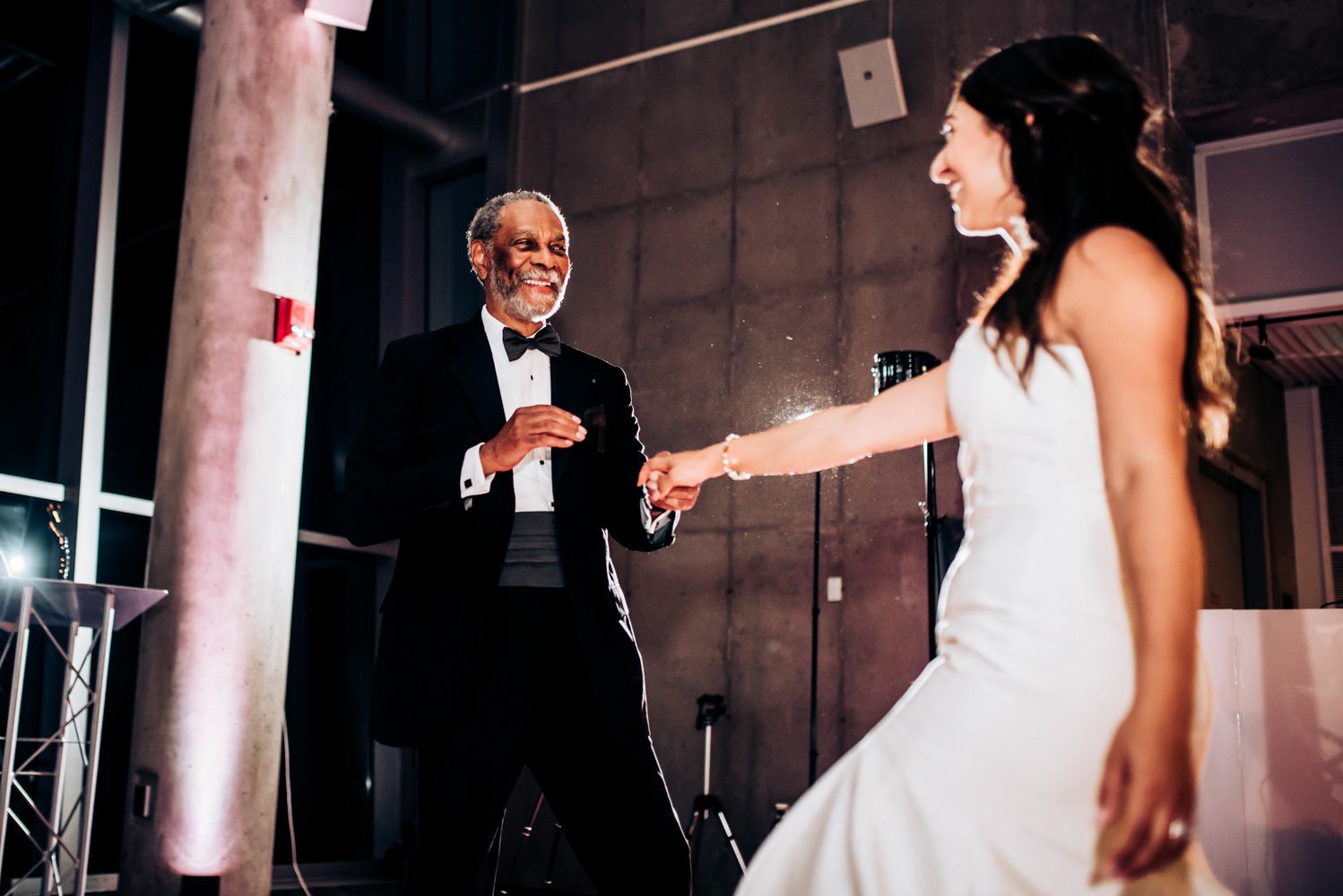 Joyful dancing moment at wedding reception with elegant white dress in focus.