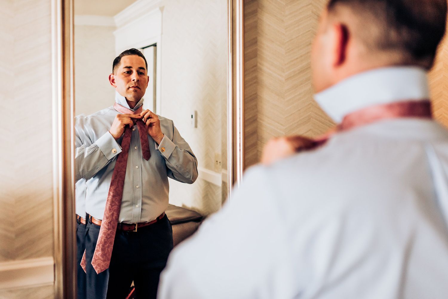 A reflection in a mirror shows someone adjusting a red bow tie while getting dressed.