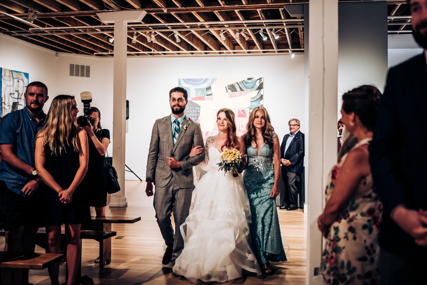 Wedding ceremony guests gather in an art gallery space while a couple walks down the aisle.