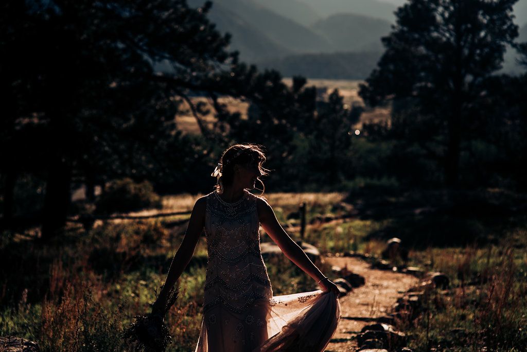 Backlit silhouette of person on mountain trail during sunset.