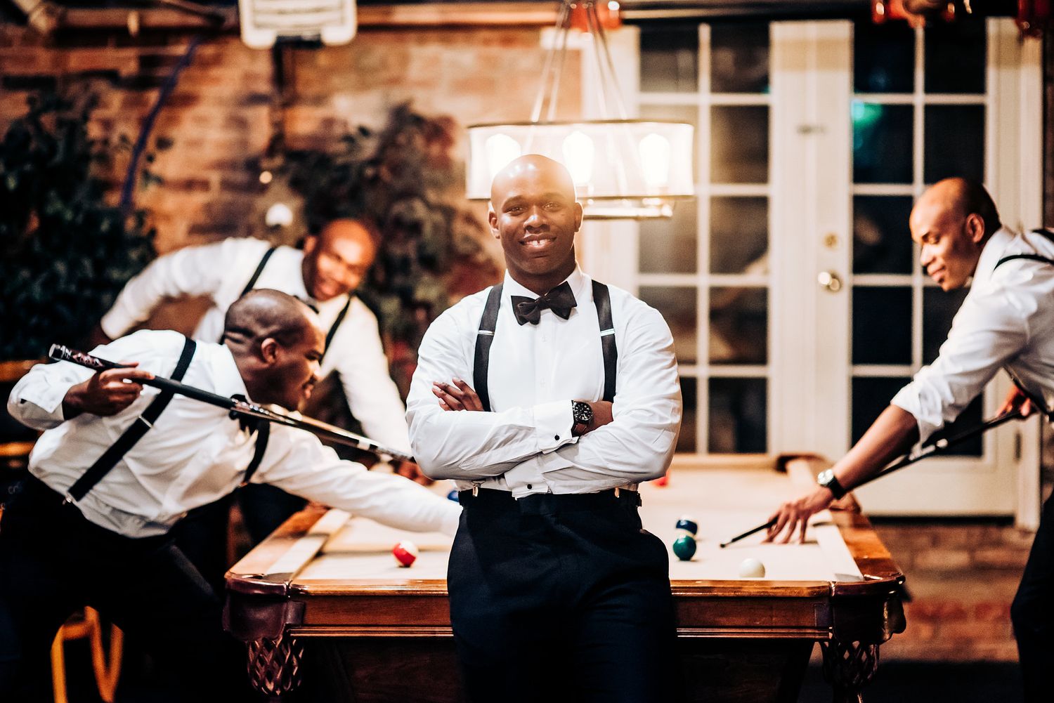 Groomsmen in suspenders and bowties pose near a wooden wall at the reception.