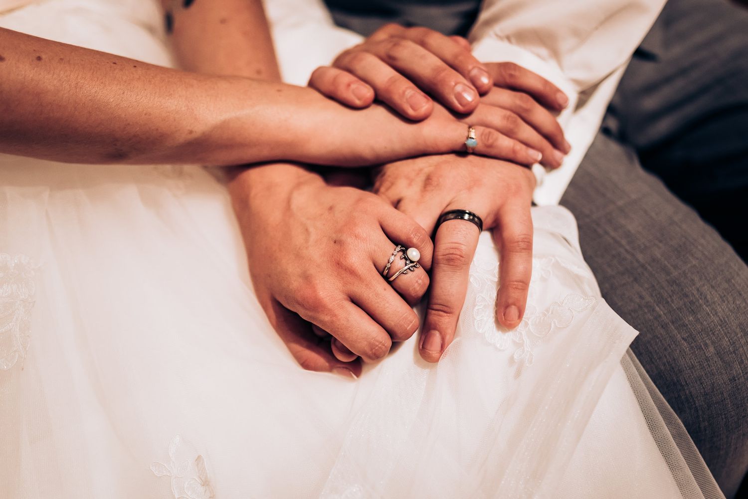 Close-up of hands with wedding rings resting on white dress fabric.