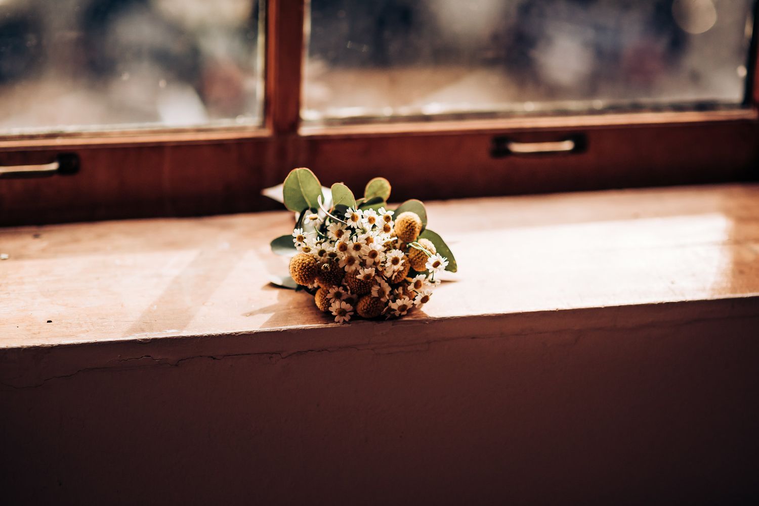 A delicate floral bouquet rests on a wooden windowsill in natural light.