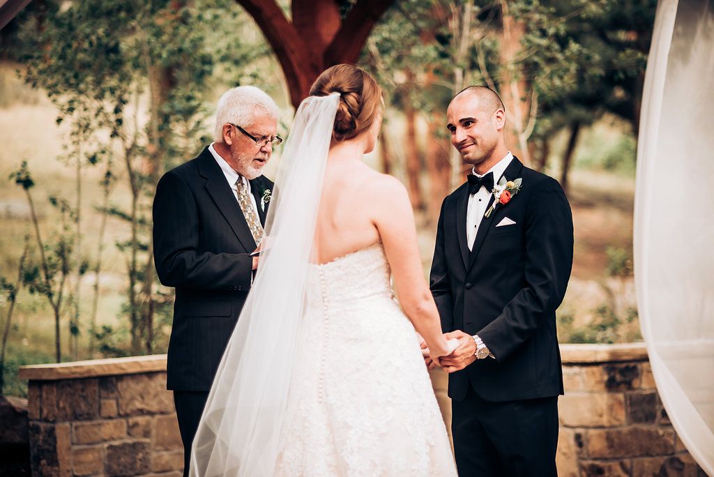 Wedding ceremony under clear skies with officiant and couple at rustic venue.
